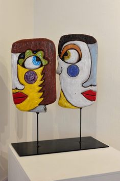 two colorful masks are on display in a white room