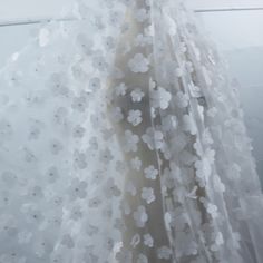 a dress with white flowers on it is hanging in front of a window and has sheer fabric