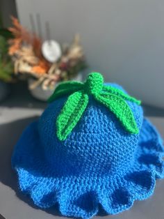 a crocheted blue hat with a green leaf on the top sits on a table