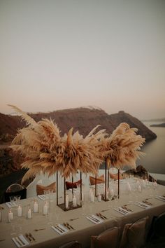 an outdoor table set up with tall vases filled with candles and pamodia