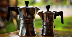 two metal coffee pots sitting on top of a wooden table