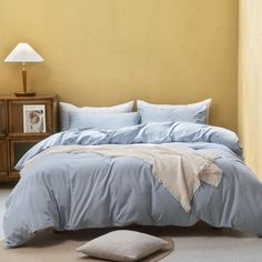 a bed with blue sheets and pillows in a room next to a lamp on a nightstand