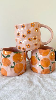 three oranges painted on ceramic mugs sitting next to each other in front of a white wall