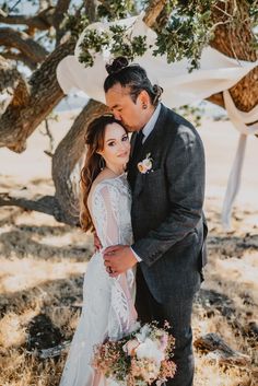 a bride and groom pose for a photo under a tree at their wedding in the desert