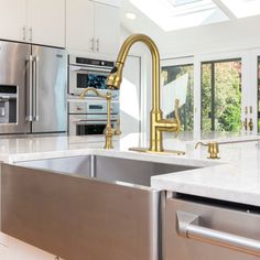 a kitchen with stainless steel appliances and white counter tops, gold faucet handles