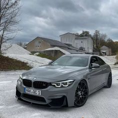 a grey car parked in front of a building on a snowy road with houses behind it