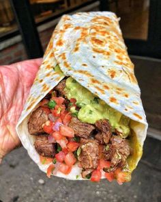 a burrito filled with meat, guacamole and tomatoes on top of it