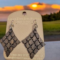 a pair of black and white earrings sitting on top of a wooden table in front of a sunset