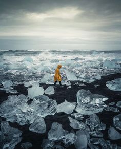 a person in yellow jacket walking on ice covered ground near the ocean with large chunks of ice