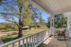 a porch with chairs and table on it next to a large tree in the yard