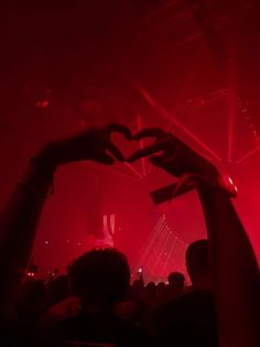 two hands making a heart shape in front of red lights at a concert or show