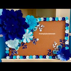 blue and white paper flowers are displayed on a bulletin board in front of a wall