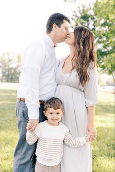 a man and woman kiss their son as he stands next to them in the grass