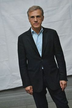 a man in a black suit and blue shirt is standing with his hands in his pockets