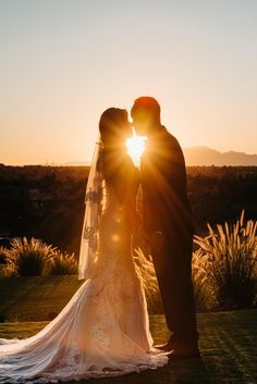 a bride and groom kissing in front of the sun