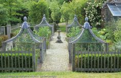 a garden with lots of plants and statues on it's fenced in area