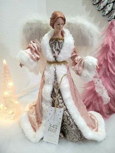 an angel figurine next to a christmas tree with pink and white feathers on it