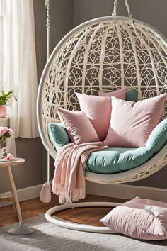 a white hanging chair with pink and blue pillows in a room next to a window