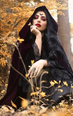 a woman with long black hair sitting in the woods