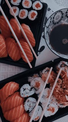 sushi and chopsticks are sitting on trays next to a bowl of sauce