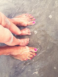 two people standing on the beach with their feet covered in sand and colored nail polish