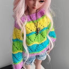 a doll with pink hair wearing a colorful sweater