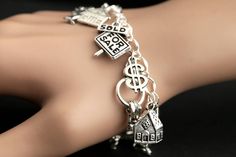 "A collection of silver plated Real Estate themed charms have been dispersed around a shimmering silver plated bracelet chain in this handmade charm bracelet. This Real Estate charm bracelet is then completed with a lobster clasp and a 1/2 inch of chain at the end for adjustable sizing. Charms in this bracelet include a \"Home Sweet Home\" door and key charm, \"Success Money Happiness\" sign post charm, house and tree plaque charm, decorative key charm, real estate word cluster coin charm, tree Silver Charm Bracelet With Vintage Charm As A Gift, Silver Vintage Charm Bracelet Gift, Silver Metal Chain Bracelet With Dangling Charms, Silver Dangle Charms Chain Bracelet, Silver Chain Bracelet With Dangle Charms, Handmade Silver Dangle Bracelets, Silver Charm Bracelet With Dangling Charms As Gift, Silver Charm Bracelet With Dangling Charms For Gift, Sterling Silver Vintage Charm Bracelet As A Gift