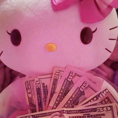 a hello kitty stuffed animal holding money in it's lap and wearing a pink bow