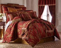 a bed with red and gold comforter set in a room next to a window