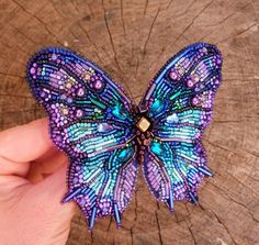 a purple and blue butterfly sitting on top of a piece of wood next to a person's hand