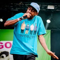 a man standing on top of a stage holding a microphone to his mouth and wearing a t - shirt that says weeze