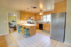 an open kitchen and dining room with tile flooring, stainless steel refrigerator and sink