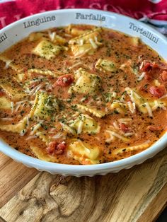 a white bowl filled with tortellini soup on top of a wooden cutting board