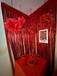 a red table topped with two vases filled with flowers next to a red curtain