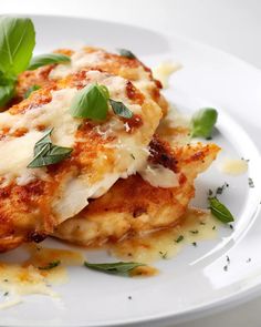 two pieces of chicken covered in cheese and herbs on a white plate with parmesan