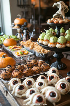 A festive Halloween dessert table featuring a variety of themed treats, including pumpkin-shaped snacks, green ice cream scoops on rice cakes, and spooky eyeball cookies. The display is decorated with pumpkins, black spiders, and a skull centerpiece, creating a fun and eerie atmosphere perfect for Halloween celebrations. Halloween Party Food Table Set Up, Halloween Birthday Party For Kids Food, Spooky Themed Food, Halloween Birthday Party Food, Halloween 3rd Birthday Party, Halloween Party Ideas For Adults Theme, Halloween Birthday Party For Adults, Adult Halloween Birthday Party, Halloween Themed Dinner