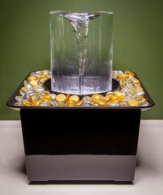 a glass vase filled with gold coins on top of a black box next to a green wall