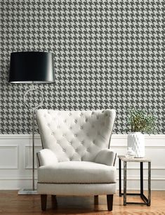 a white chair sitting next to a lamp on top of a hard wood floor in front of a black and white wall