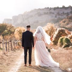 a bride and groom walking down a dirt road