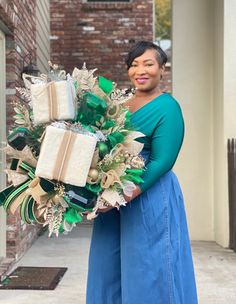 a woman is standing outside holding a christmas wreath with presents wrapped in green and gold