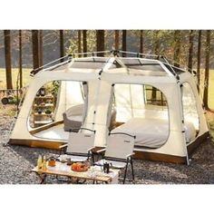 a tent set up in the woods with two chairs and a coffee table on it