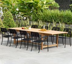 an outdoor dining table with black chairs and plants in the backgroung area