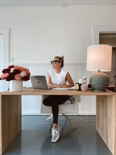 a woman sitting at a desk with a laptop computer in front of her and flowers on the table