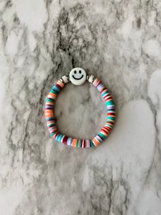 a bracelet with a smiley face and multicolored beads on top of a marble surface