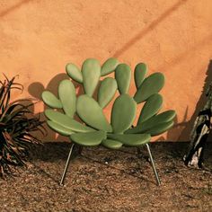 a green chair sitting on top of a dirt ground next to a plant potted in front of a wall