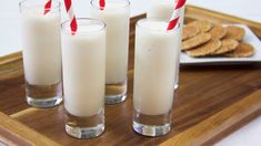 three glasses filled with milk sitting on top of a wooden tray next to crackers