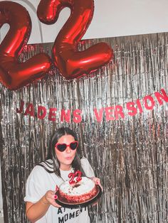 a woman holding a cake in front of a backdrop with the number twenty two on it