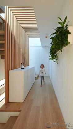 a woman walking down a hallway next to a plant hanging from the ceiling above her head