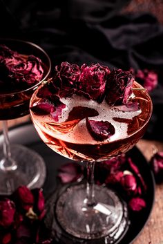 two wine glasses filled with rose petals on top of a black plate next to each other