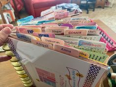 a person holding an open book in front of a pile of books on a table